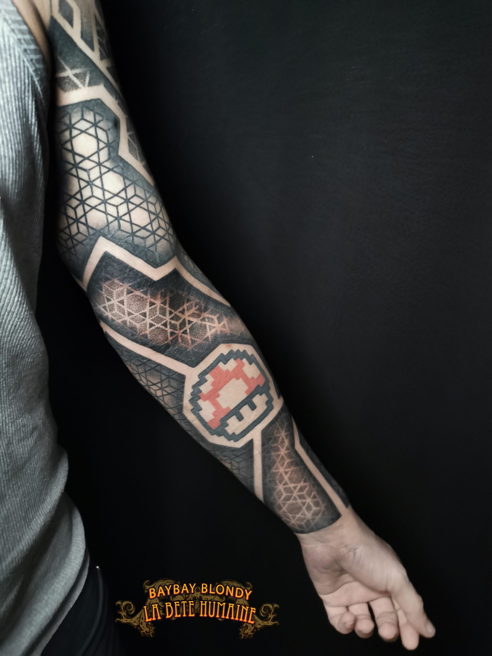 Baybay Blondy, tatoueuse guest à Paris - Bras géométrique réhaussé d’un champignon de Super Mario tatoué par son confrère Bro Vanthorn