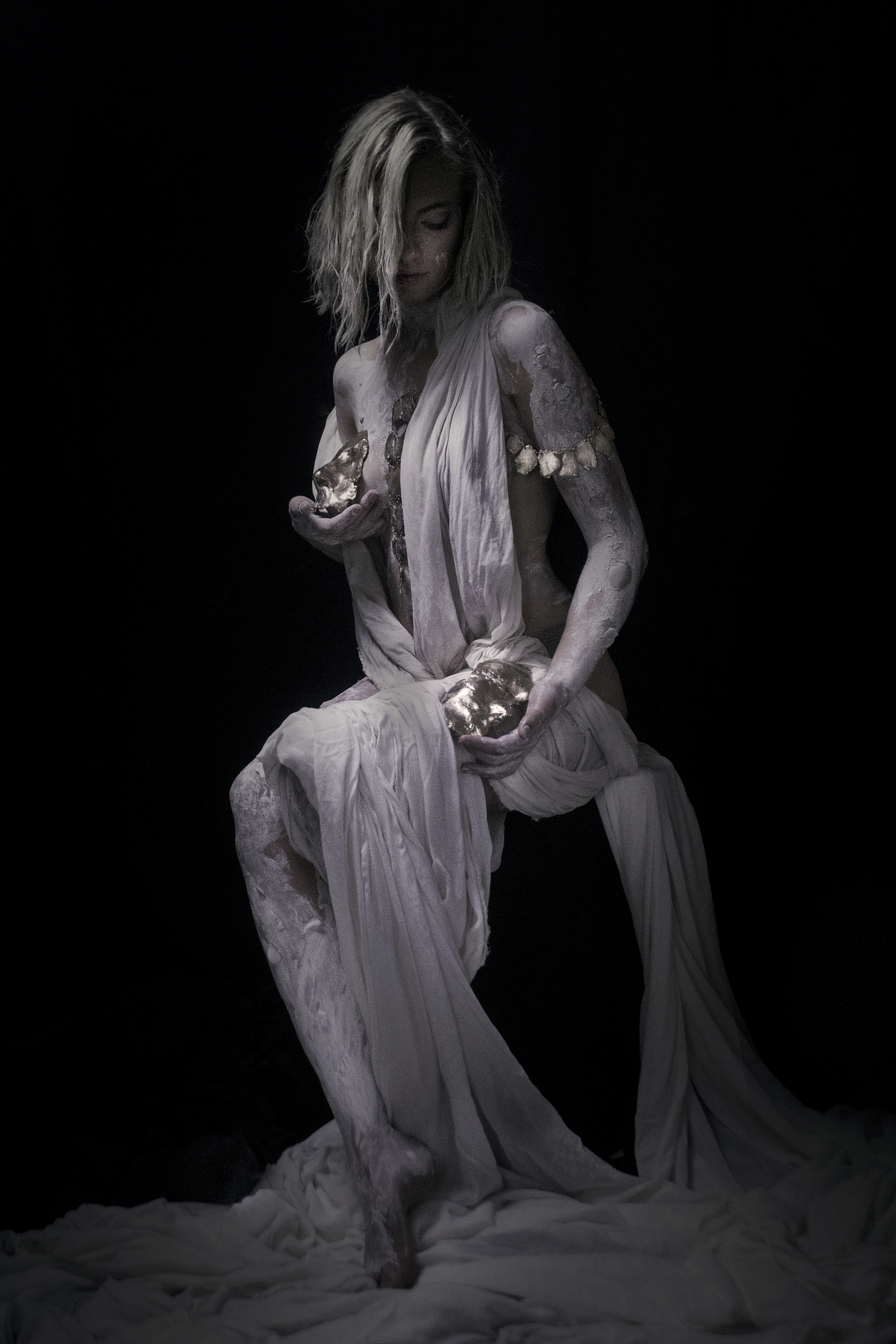 Photographie artistique d’un corps féminin drapé de tissu clair, tenant des éléments minéraux, réalisée par Michka Kovalsky.