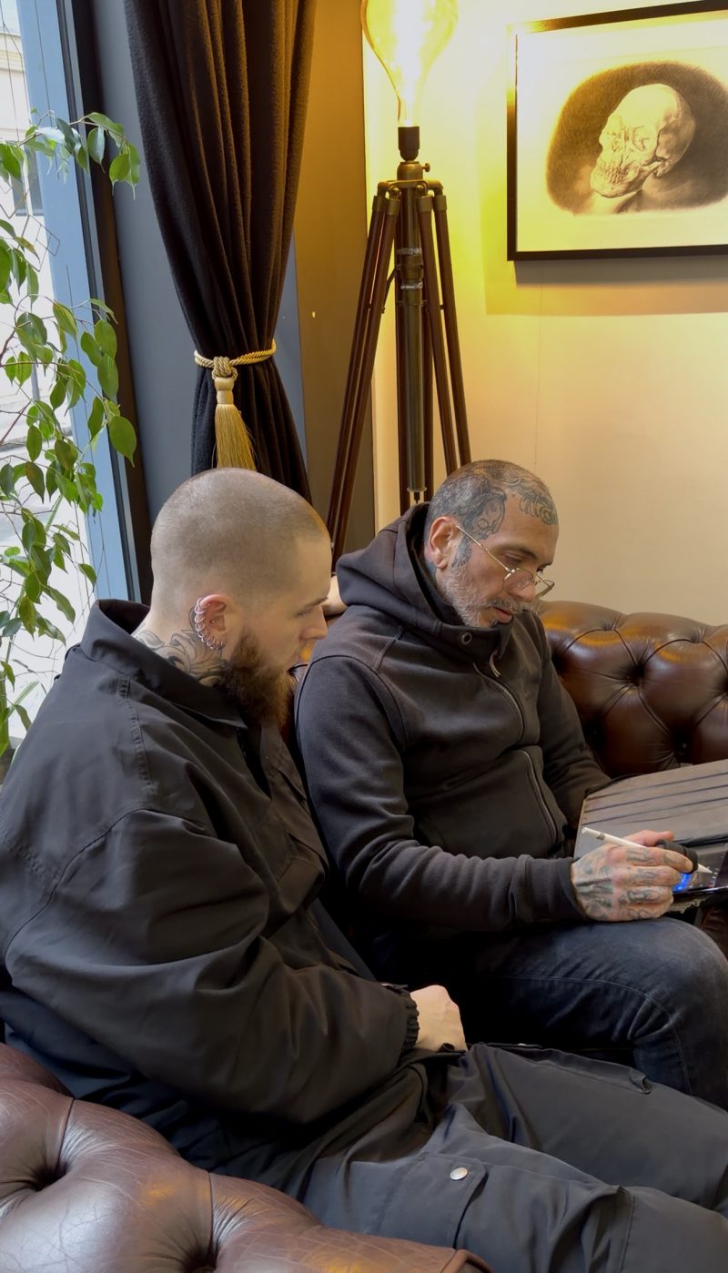 Tattoo artist and client discussing a realism tattoo design on a tablet during a consultation in a Paris tattoo studio.