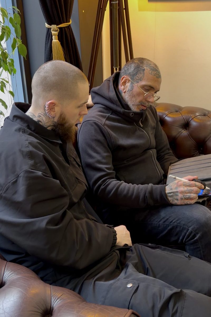 Tattoo artist and client discussing a realism tattoo design on a tablet during a consultation in a Paris tattoo studio.