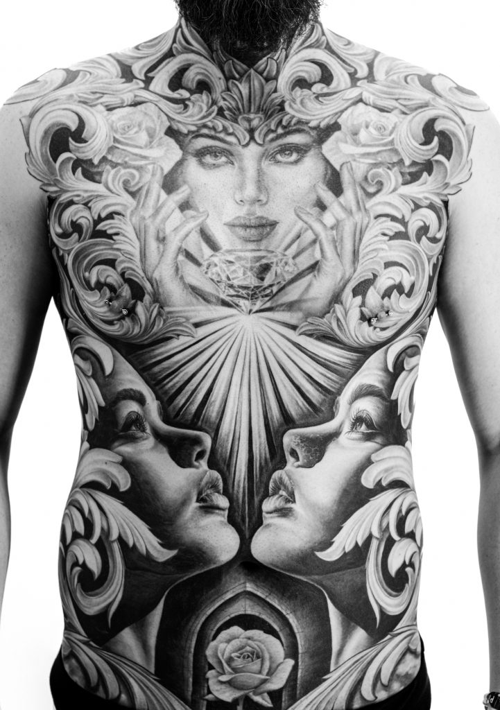 Realism chest tattoo featuring a female portrait holding a diamond, surrounded by roses and ornamental acanthus leaves.