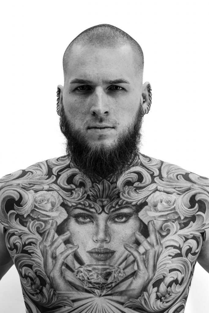 Willis - tattooed man with a detailed realism chest tattoo of a female portrait framed by ornamental leaves and roses.